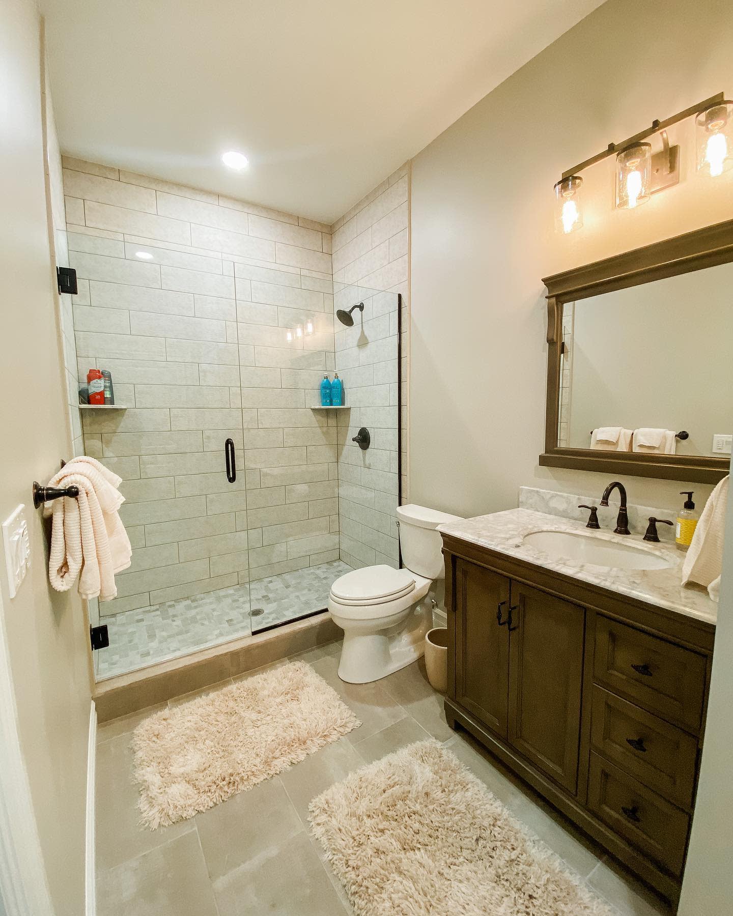 Simple modern bathroom with glass shower, wooden vanity, and beige tile flooring.